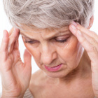 Eine ältere Frau hält sich die Hände an die schlefen, klagt über Kopfschmerzen und Depressionen