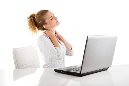 Junge Frau zieht am Schreibtisch vor ihrem Laptop und hat Schmerzen im Nacken